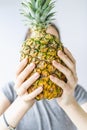 Girl holding a pineapple in front of her face over white background. Raw eating concept Summer and vacantion time.