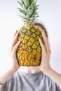 Girl holding a pineapple in front of her face over white background. Raw eating concept Summer and vacantion time.