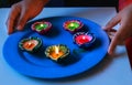 A girl holding a plate of Colourful lit diyas/lamps to celebrate diwali