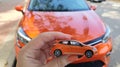 Girl holding small orange car toy against real car of same type Royalty Free Stock Photo