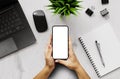 A girl holding a smartphone blank screen with a laptop and office items on desk - top view Royalty Free Stock Photo