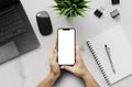 A girl holding a smartphone blank screen with a laptop and office items on desk - top view Royalty Free Stock Photo