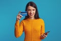 Girl holding smartphone and plastic credit card isolated over blue background Royalty Free Stock Photo