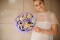 Girl holding a spring bouquet of tender color creamy color flowers with leaves in a purple paper Royalty Free Stock Photo