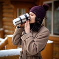 A girl holding a thermos with a hot drink. A mug of coffee in her hands. Winter alley in the city, a young girl walks