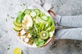 Girl holding vegan, detox Buddha bowl with quinoa, avocado, zucchini noodles, cucumber, tomato, lime, kiwi, tofu, spinach