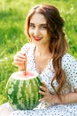 Girl is holding watermelon with cocktail straw on green nature background.