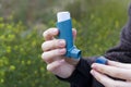 A girl holds an asthma inhaler against a background of blooming