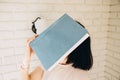 The girl holds a big blue book in her hand and covers her face against the background of a white brick wall Royalty Free Stock Photo