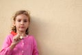 Girl holds big pencil, stands near wall