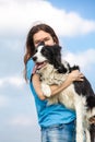A girl holds a black and white border collie dog in her hands and hugs and smiling. Portrait against a bright blue sky Royalty Free Stock Photo