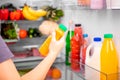 A girl holds a bottle of orange vegetable or fruit juice against the background of an open refrigerator with food. Concept of