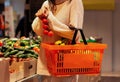 Girl holds a branch of tomatoes in her right hand and a basket  full of fruits in her left hand in a supermarket Royalty Free Stock Photo