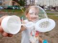 The girl holds a bubble and looks through it in the playground