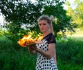 Girl holds a burning book in her hands. A young woman in a forest burns a book