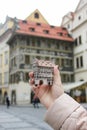 Girl holds czech souvenir house Minute House, Dum u Minuty, on background of that real house, Old Town Square