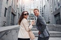 Girl holds drink. Woman and man in the town at daytime. Well dressed people