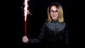 The girl holds a fireworks in a hand. A young woman is standing in a shiny evening dress on a black background. 4k