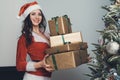 Girl holds four gifts in a gold wrapper in an apartment decorated for the new year. Young woman in red Santa Claus costume pulls Royalty Free Stock Photo