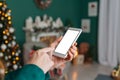 Girl holds her finger in front of smartphone mockup screen. against the background of New Year`s and Christmas cozy interior Royalty Free Stock Photo