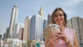 The girl holds in her hands the money of the United Arab Emirates on the background of the city center of Dubai. Royalty Free Stock Photo