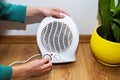 A girl holds her hands near a plastic fan heater and warms her hands, adjusting the temperature at home, close-up Royalty Free Stock Photo