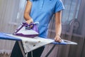 The girl holds an iron on an ironing board with a ferry and irons things. Cleaning service of the apartment. Blue T-shirt and Royalty Free Stock Photo