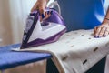 The girl holds an iron on an ironing board with a ferry and irons things. Cleaning service of the apartment. Blue T-shirt and Royalty Free Stock Photo