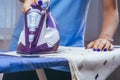 The girl holds an iron on an ironing board with a ferry and irons things. Cleaning service of the apartment. Blue T-shirt and Royalty Free Stock Photo