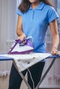 The girl holds an iron on an ironing board with a ferry and irons things. Cleaning service of the apartment. Blue T-shirt and Royalty Free Stock Photo