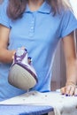 The girl holds an iron on an ironing board with ferry and irons things. Cleaning service of the apartment. Blue T-shirt and young Royalty Free Stock Photo