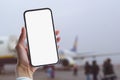 Girl holds a mock-up of a smartphone with a white screen close-up. Phone on the background of the airport with an airplane