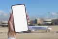 Girl holds a mock-up of a smartphone with a white screen close-up. Phone on the background of the airport with an airplane