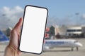 Girl holds a mock-up of a smartphone with a white screen close-up. Phone on the background of the airport with an airplane