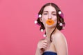 A girl holds a mouthful of paper lips on a stick. On a pink background.