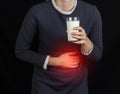 The girl holds onto her stomach and holds a glass of milk, a black background, pain and heartburn in her stomach