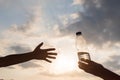 Girl holds out plastic bottle with crystal clear mineral water to woman. Two hands opposite the rays of the sunset sky. Concept. Royalty Free Stock Photo