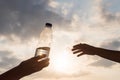 Girl holds out plastic bottle with crystal clear mineral water to woman. Two hands opposite the rays of the sunset sky. Concept. Royalty Free Stock Photo