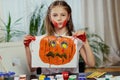 A girl holds a poster with painted Halloween pumpkin.