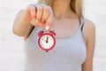 The girl holds a red alarm clock on the outstretched hand against the background of a white brick wall Royalty Free Stock Photo