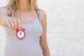 The girl holds a red alarm clock on the outstretched hand against the background of a white brick wall Royalty Free Stock Photo