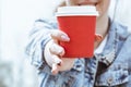 A girl holds a red paper cup of coffee. Glass of coffee close-up in hand