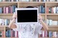 Girl holds tablet to cover her face in library Royalty Free Stock Photo