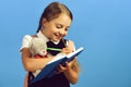 Girl holds teddy bear and writes in blue notebook Royalty Free Stock Photo