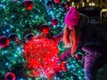 A girl holds on to a giant Christmas ball with garlands hanging on a large Christmas tree