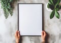 Girl holds a white poster mockup in her hands with green plants around on concrete gray background Royalty Free Stock Photo