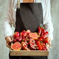 Girl holds wooden tray with fresh red vegetables and fruits on grey background. Healthy eating vegetarian concept. Royalty Free Stock Photo