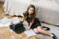 A girl in a holiday dress writes a letter to Santa Claus on an old typewriter on the floor Royalty Free Stock Photo