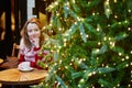 Girl in holiday sweater drinking coffee or hot chocolate in cafe decorated for Christmas Royalty Free Stock Photo