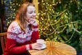 Girl in holiday sweater drinking coffee or hot chocolate in cafe decorated for Christmas Royalty Free Stock Photo